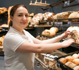 Bäckereifachverkäuferin steht im Laden am Brotregal