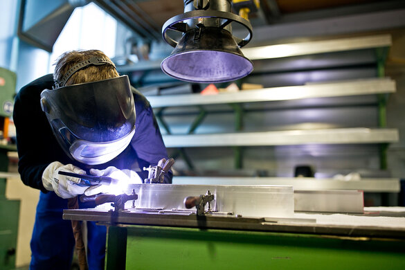  Metallbauer mit Schutzausrüstung schweißt mit Schweißgerät ein Metallbauteil zusammen